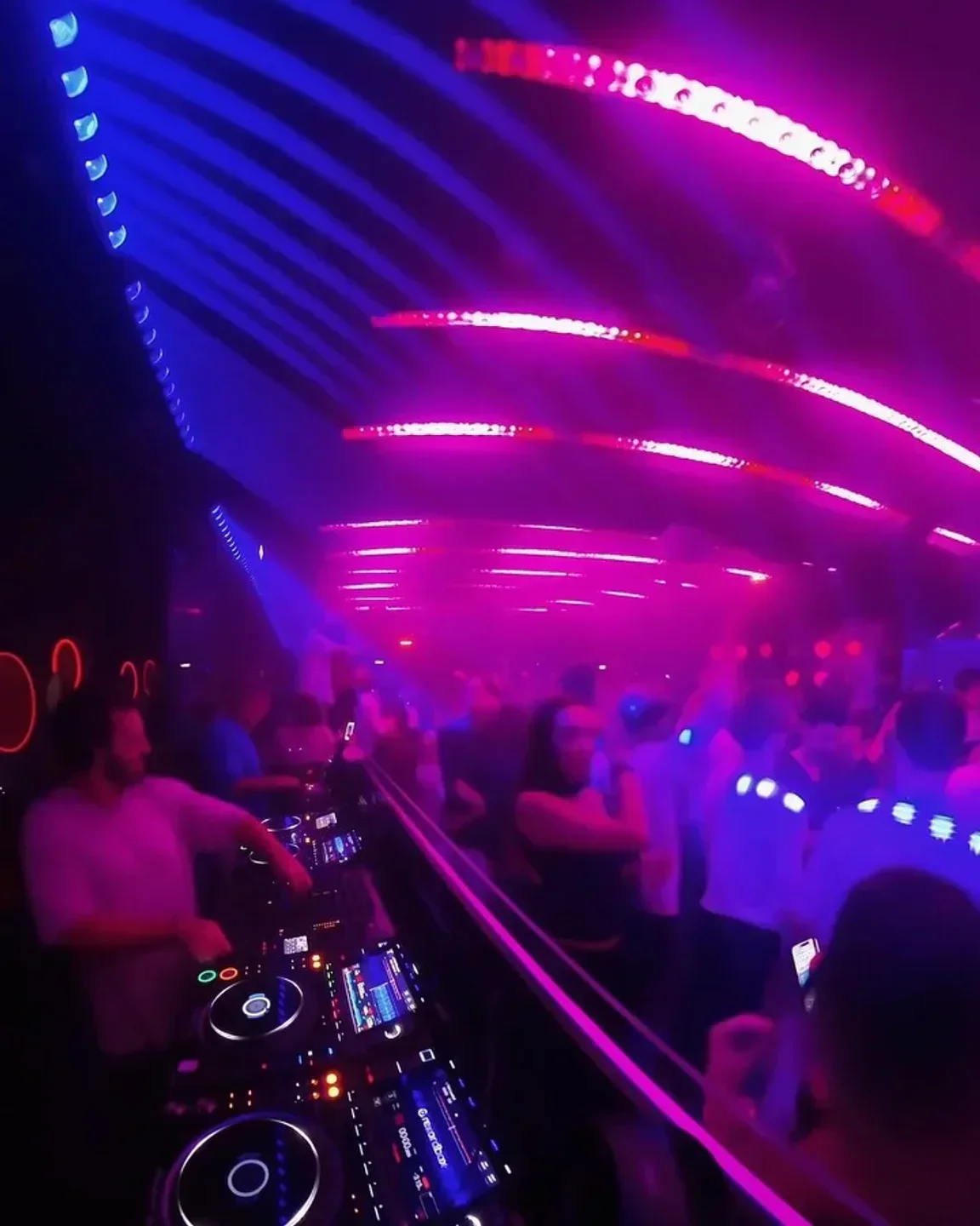 DJ mixing at Bisous Bisous nightclub in Cannes, with vibrant pink and blue lighting.