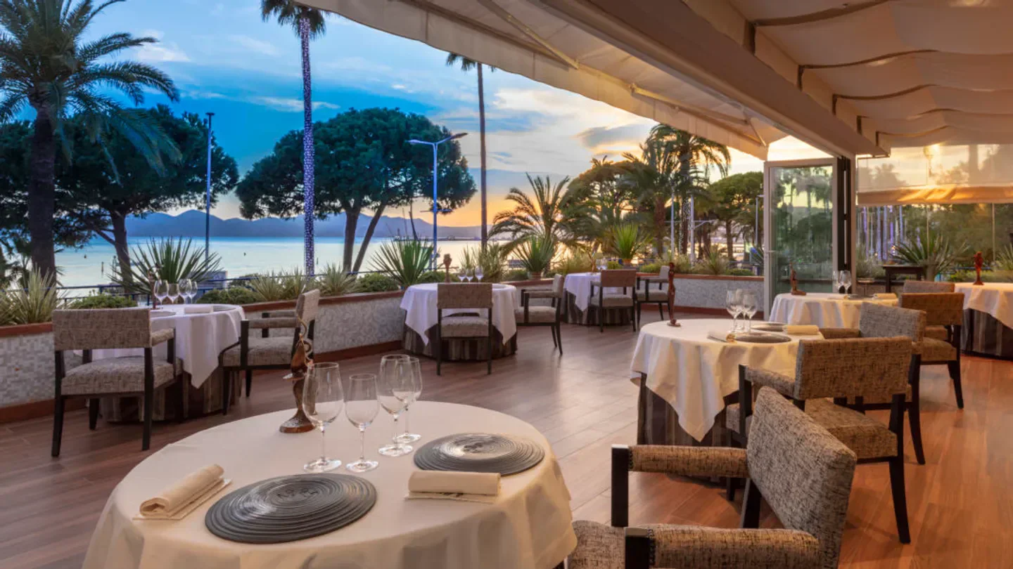 Outdoor dining at La Palme d'Or in Cannes, with tables set and ocean views at sunset.