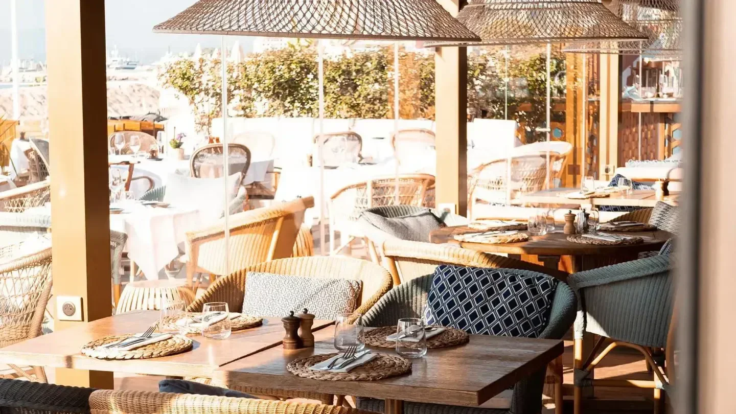 Beach club dining in Long Beach, Cannes. Stylish setting with woven chairs and tables.