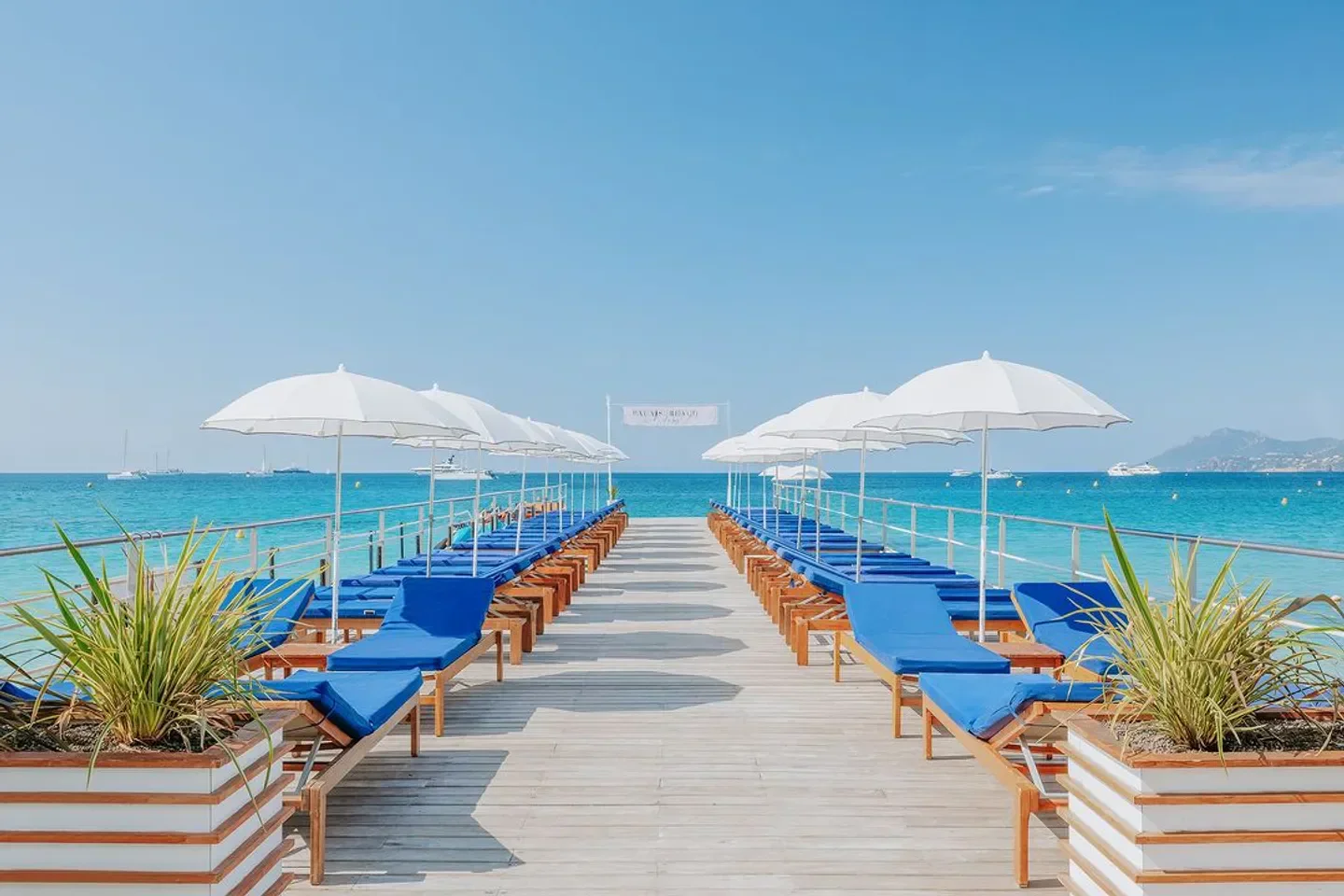 Palais Stéphanie Beach in Cannes: blue lounge chairs, umbrellas, and ocean views.